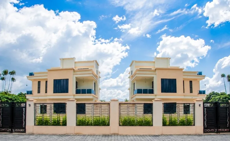 Two matching Neema Court maisonettes behind a modern gated perimeter wall under a blue sky